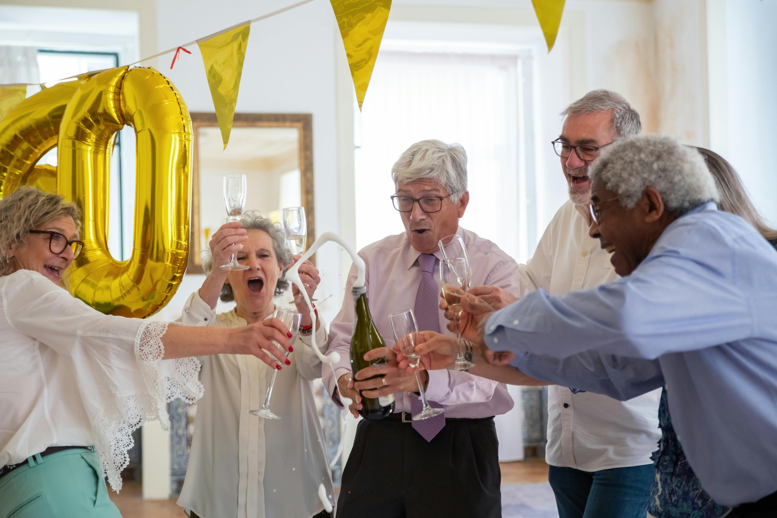 A group of seniors celebrate indoors with champagne, smiles, and festive decorations, highlighting joy and friendship.